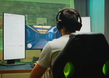 back view professional gamer streaming his competition triple monitor setup with two streaming chats open (1)