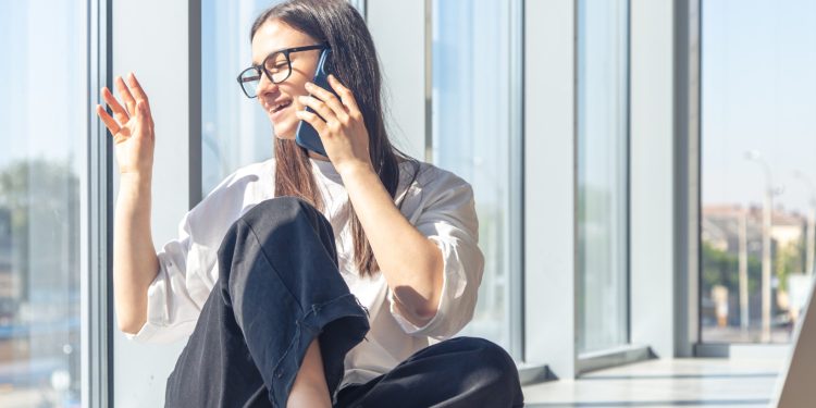 young woman glasses is talking smartphone near window (1)